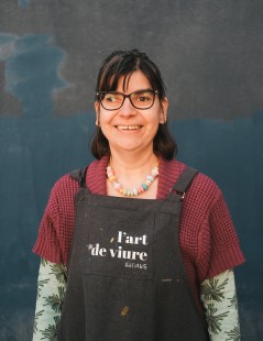 foto de Gemma Bueno, artista de l’Art de Viure, sonriendo y llevando un delantal con el logo del taller inclusivo y un collar con piezas de colores