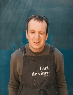 foto de Ruben Romero, artista de l’Art de Viure, llevando un delantal con el logo del taller inclusivo. Sonriendo nos guiña el ojo